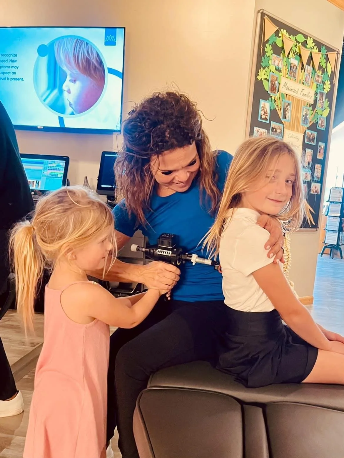 Dr. Sandie McCuiston using a gentle chiropractic activator with children nearby